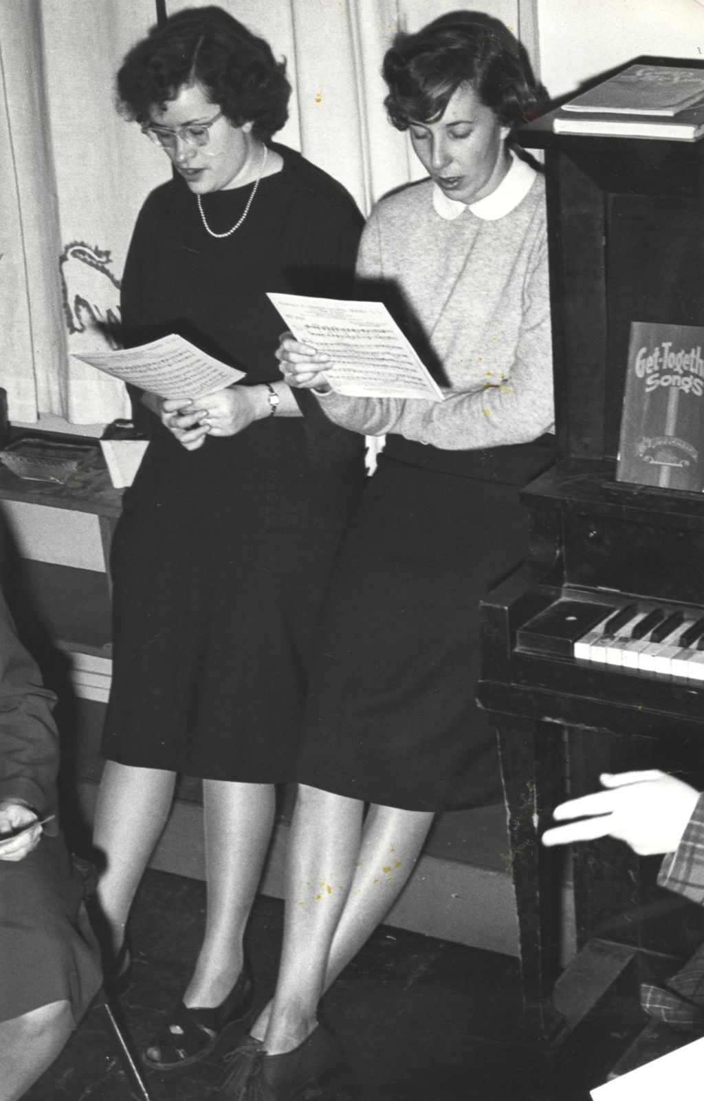 Two young women singing next to piano