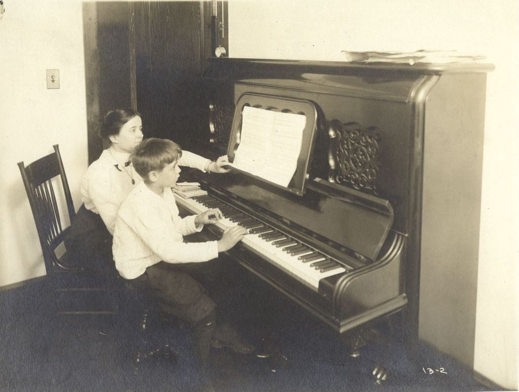 Boy playing piano with teacher watching