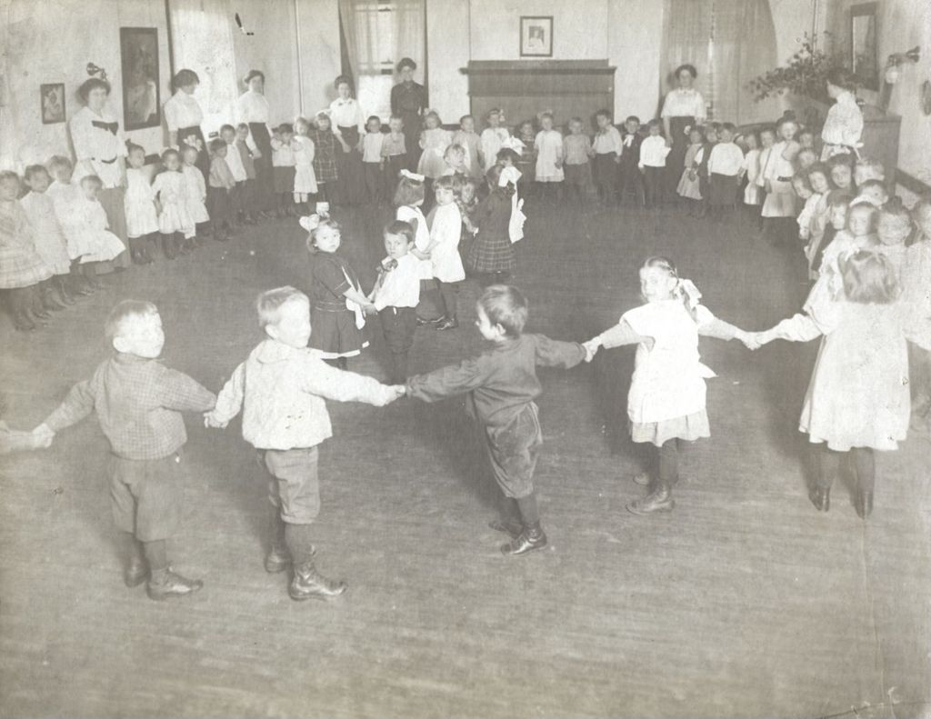 Children dancing in a circle with women watching