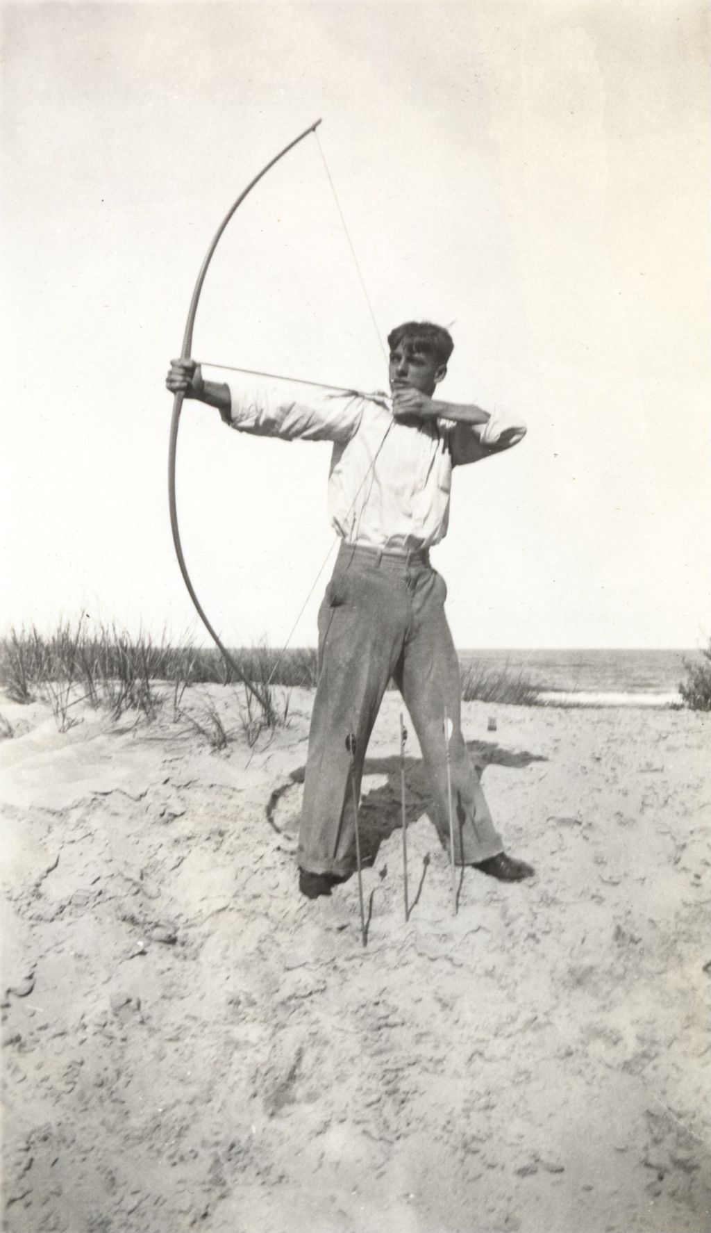Teenage boy practicing archery on a lakeshore