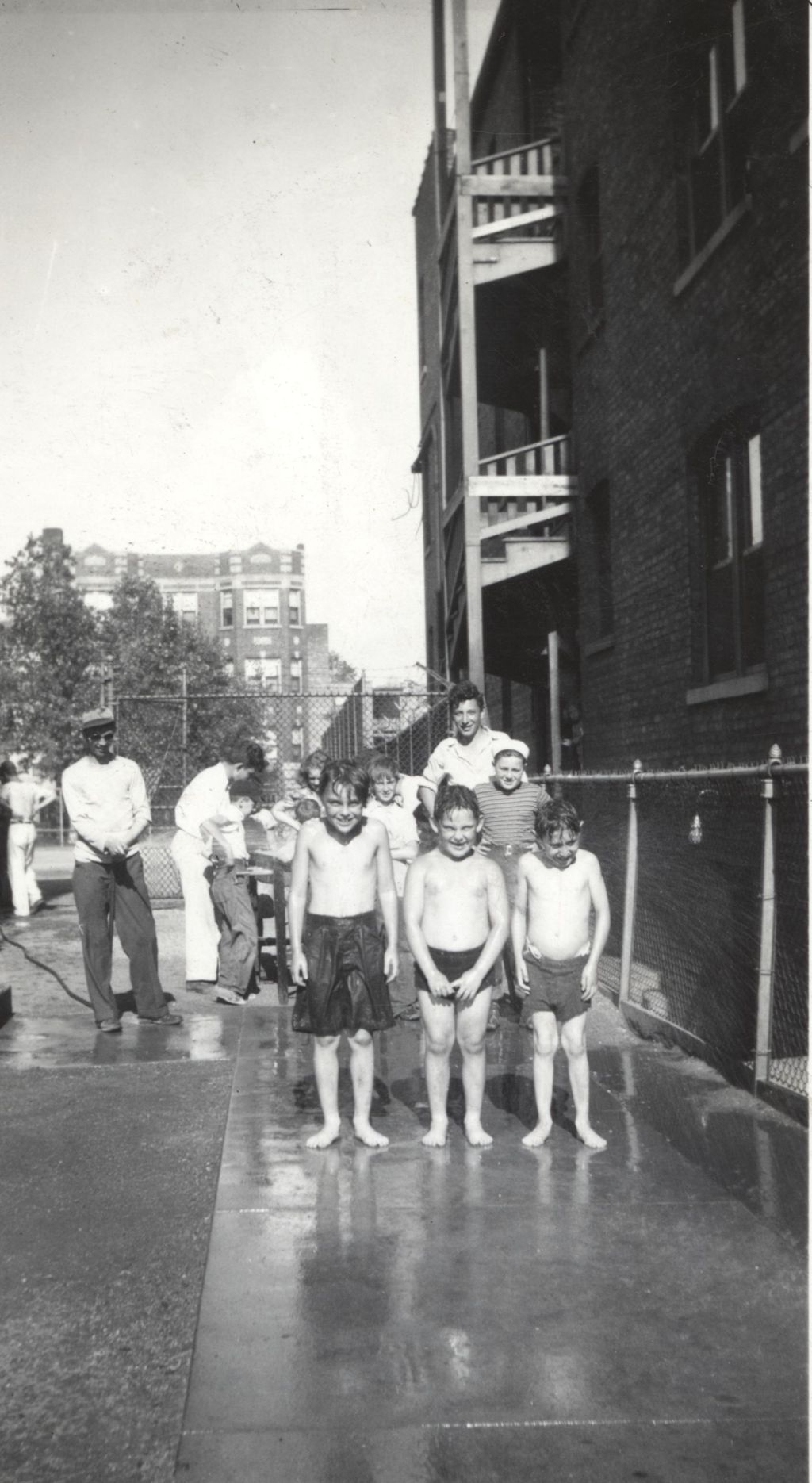 Three boys in bathing suits being sprayed with garden hose