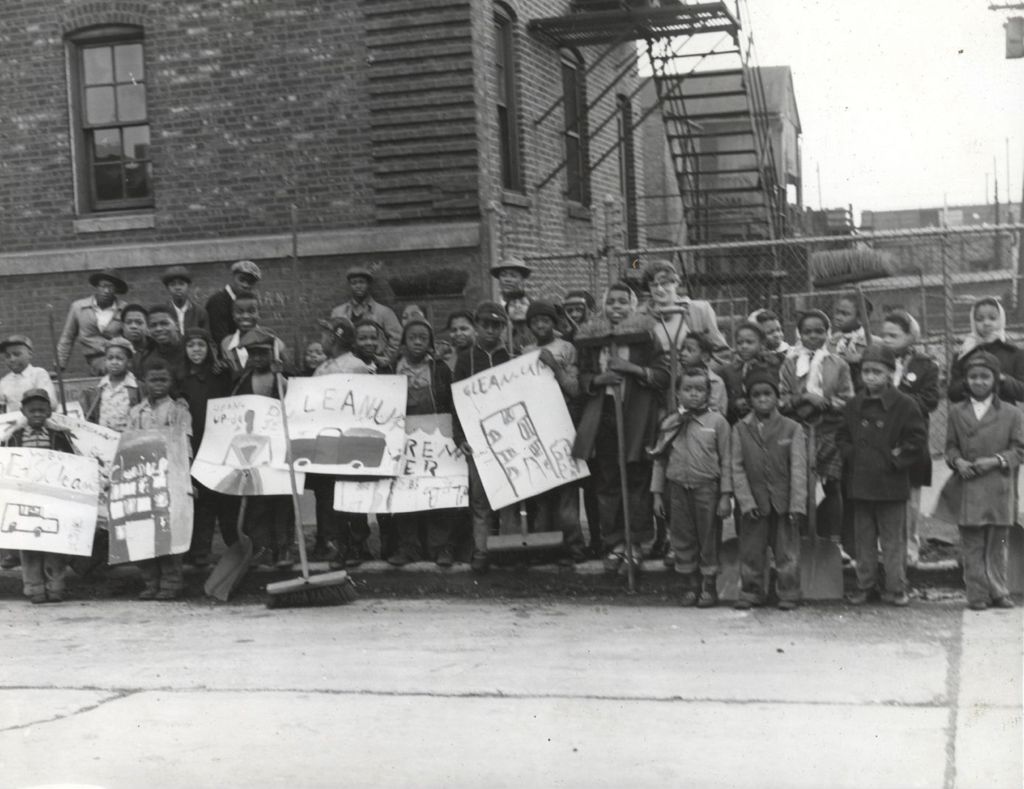 Children holding brooms and cleanup signs at Henry Booth House