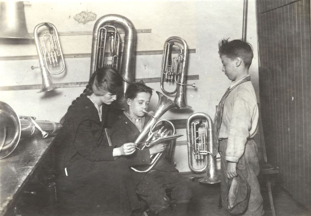 Boy playing French horn with instructor looking on