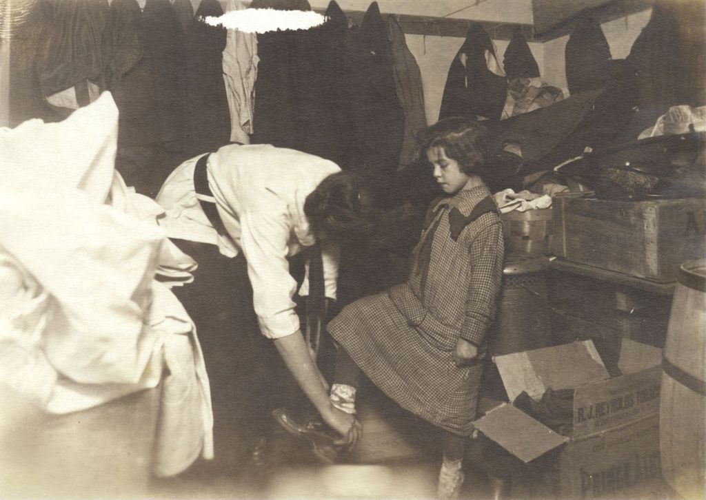 Miniature of Girl being fitted for boots in a supply storeroom