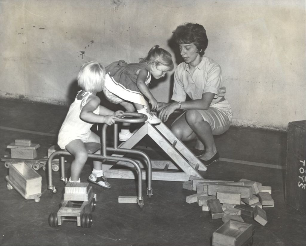 Two girls playing with toys with a woman watching