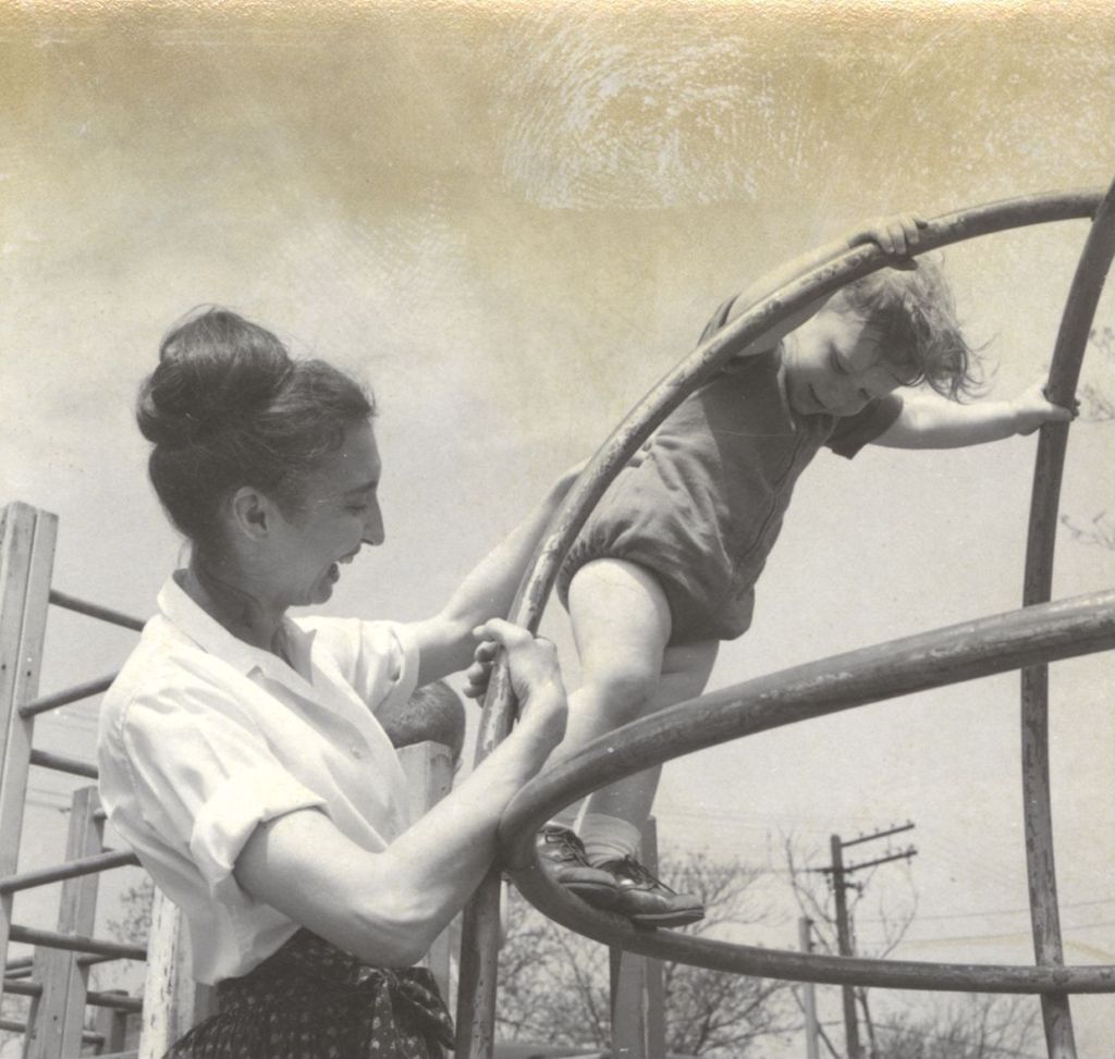 Miniature of Young girl balancing on a jungle gym with the help of a woman