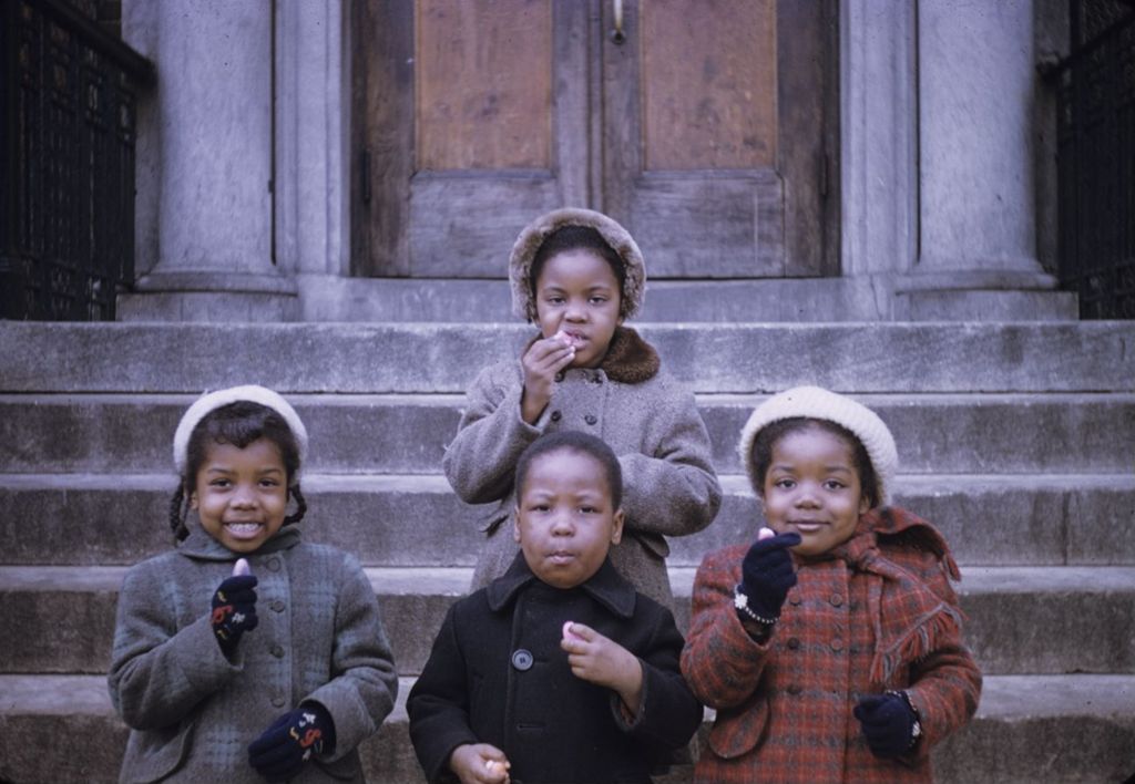 Four African American children eating snacks in front of building