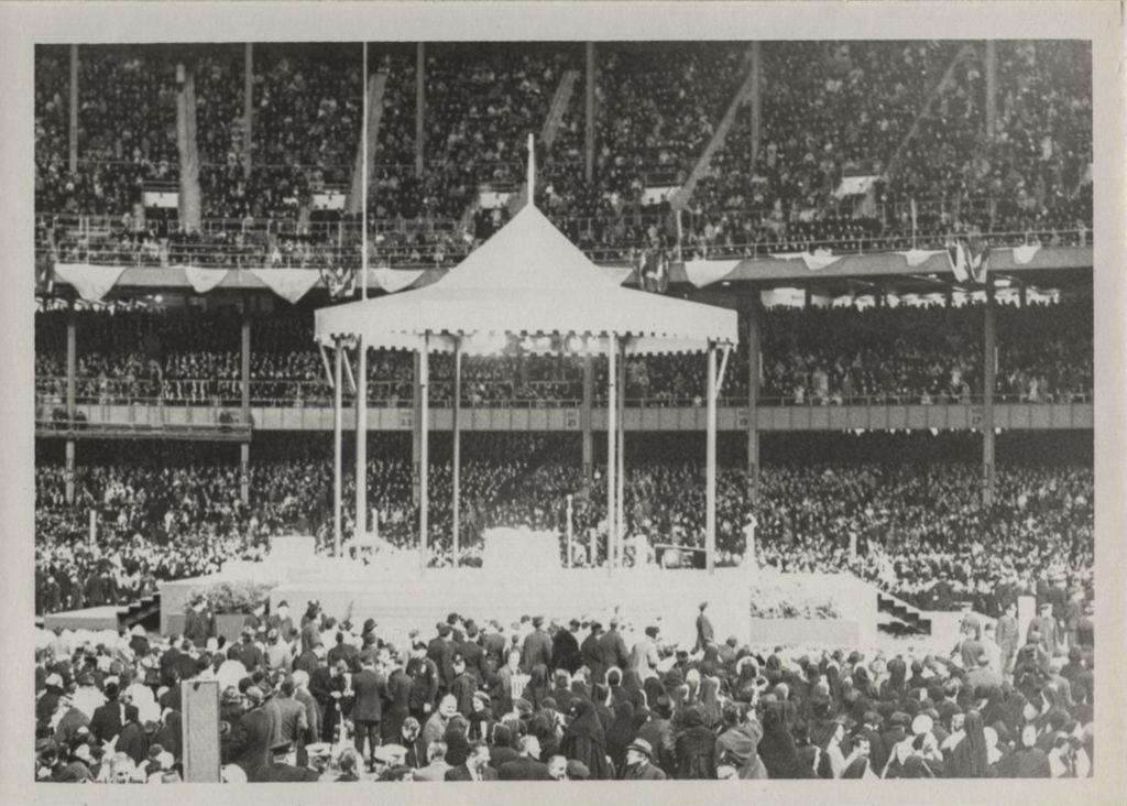 Crowd in a large stadium with speaker's pavilion at center