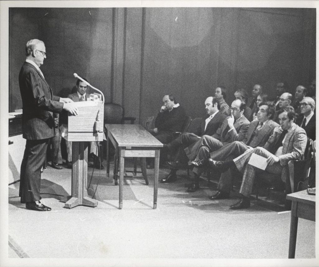 Man giving a speech to an audience including Michael, William, John, and Richard M. Daley