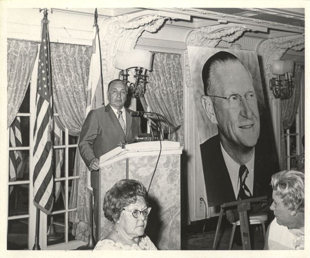 Richard J. Daley speaking at a podium next to a large photo of William McFetridge