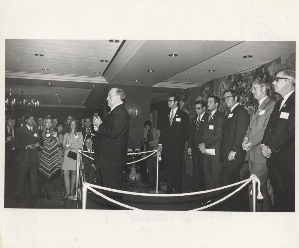 Miniature of Richard J. Daley standing with a microphone in hand at a "We Care" event