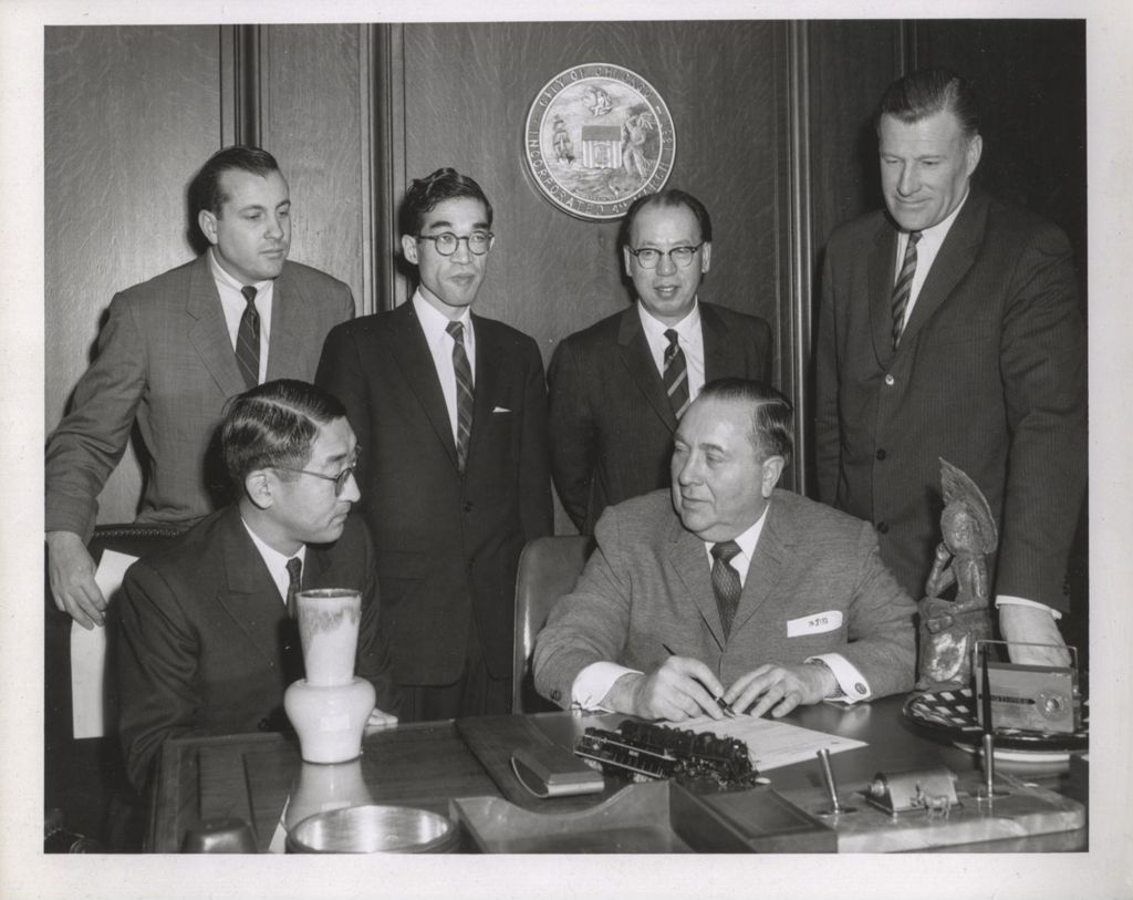 Richard J. Daley signs a document at his desk with three Asian men observing
