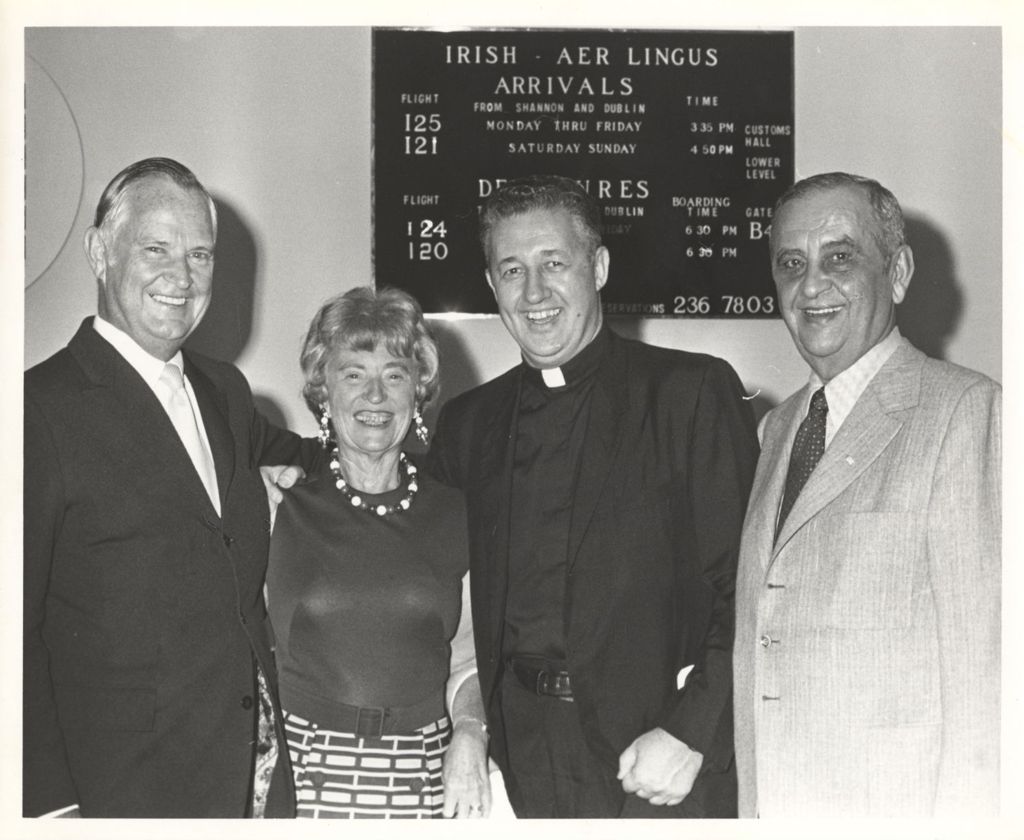 Father Graham with others in front of a sign listing Aer Lingus flights to Chicago