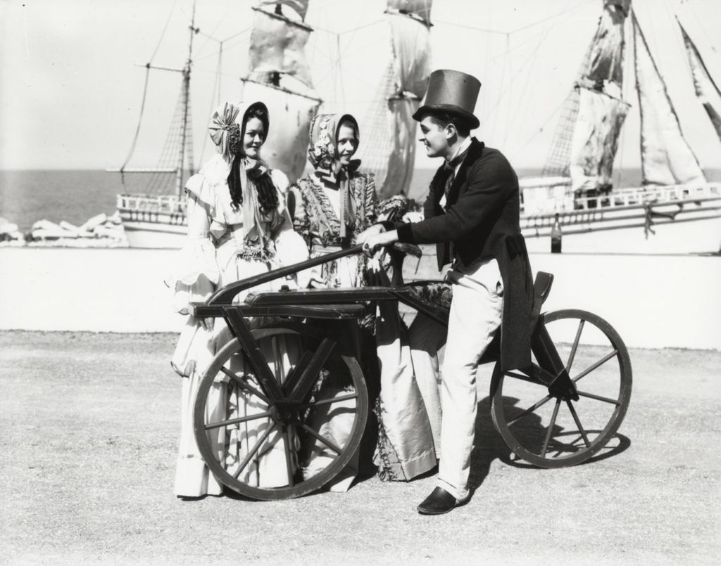 Miniature of Performers in period costume at the Century of Progress Pageant of Transportation. The man in the foreground is riding a nineteenth-century bicycle.