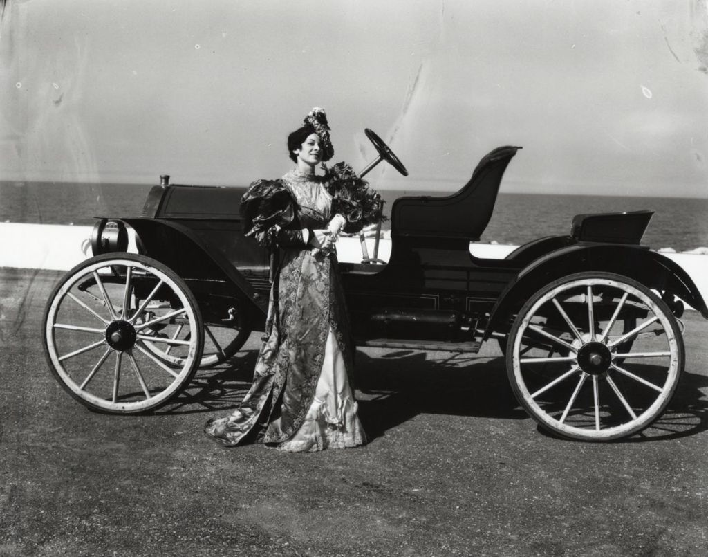 Miniature of Woman in period costume standing next to a Ford Model T