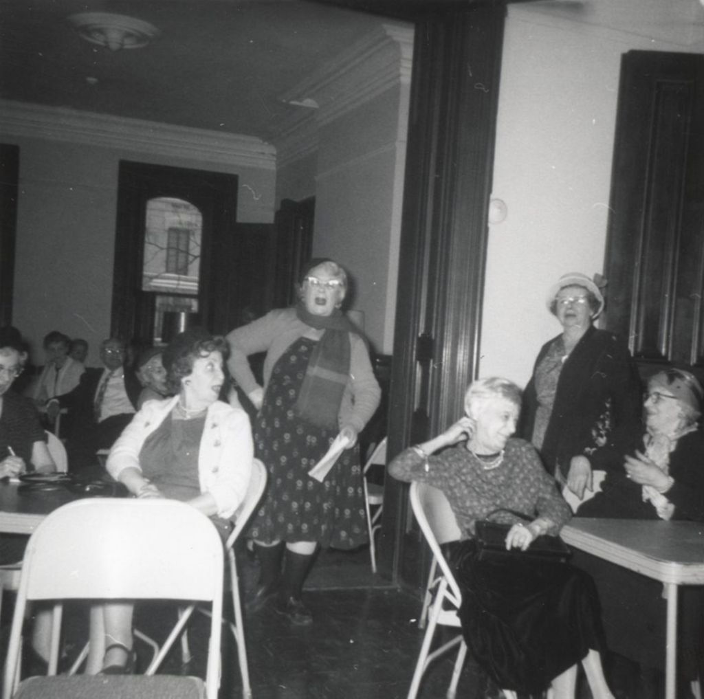 Woman speaking or performing with several other seniors looking on