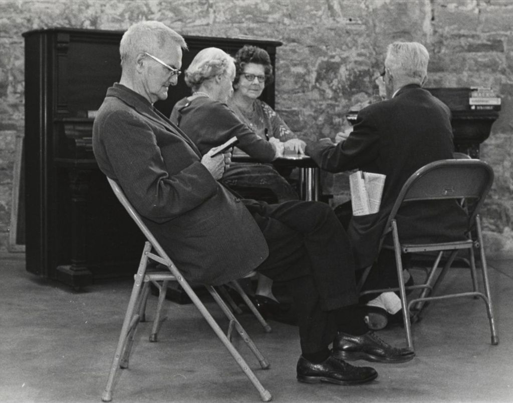A man reading a book at a senior center with other seniors playing cards in the background