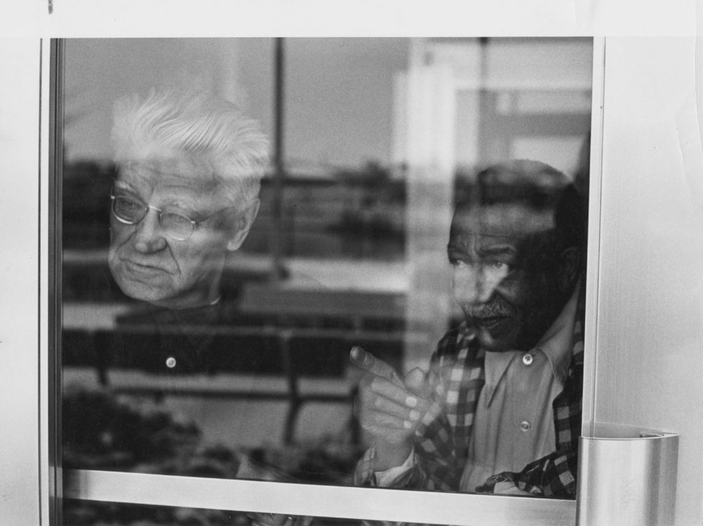 Two men looking outside from behind a glass door at the Conrad Senior Center