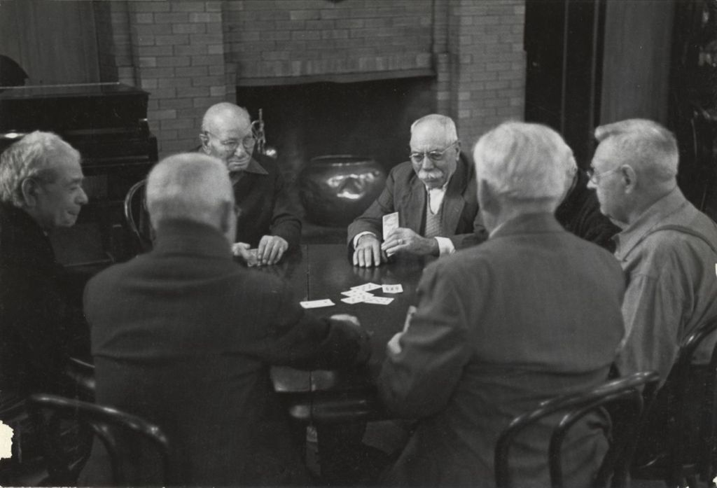 Seven men, members of the "Young Old Timers" sitting and playing cards at a table