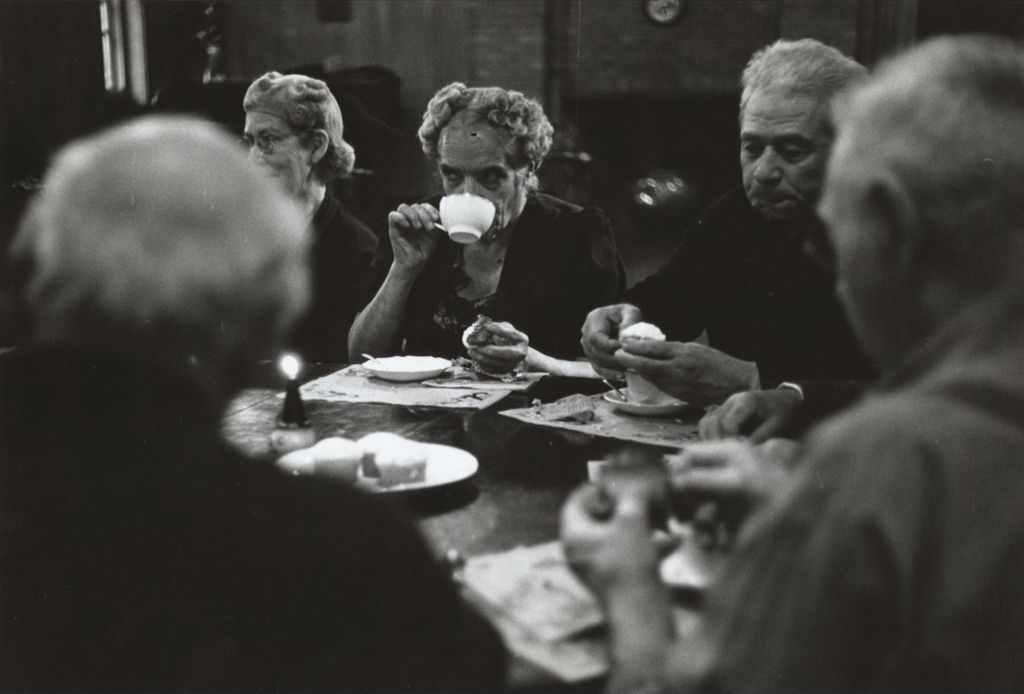 A woman sips tea or coffee from a cup during a Hull-House senior citizens club meeting in the Residents Dining Hall