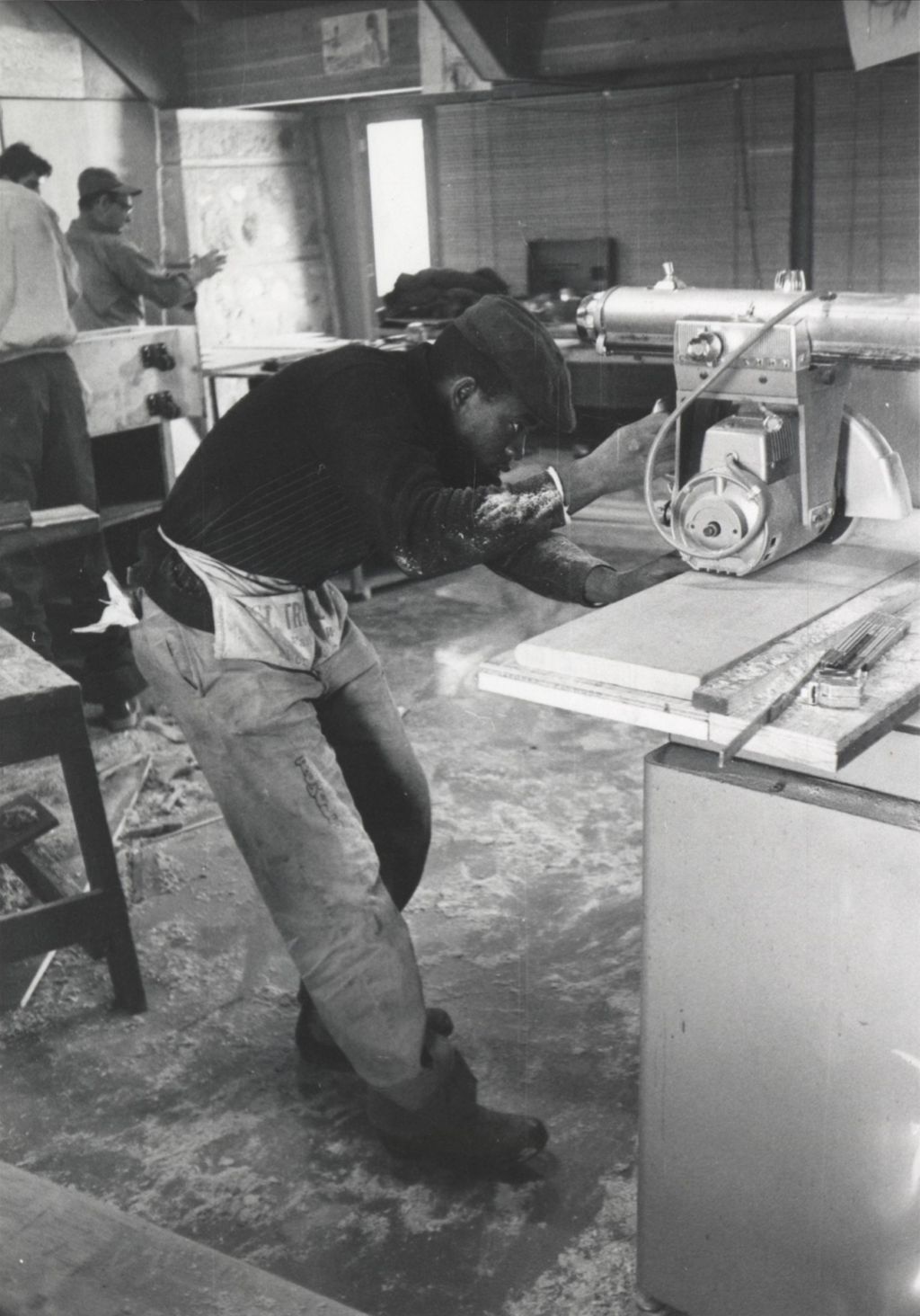 Young man using a table saw in a room at the Hull-House camp in Wisconsin