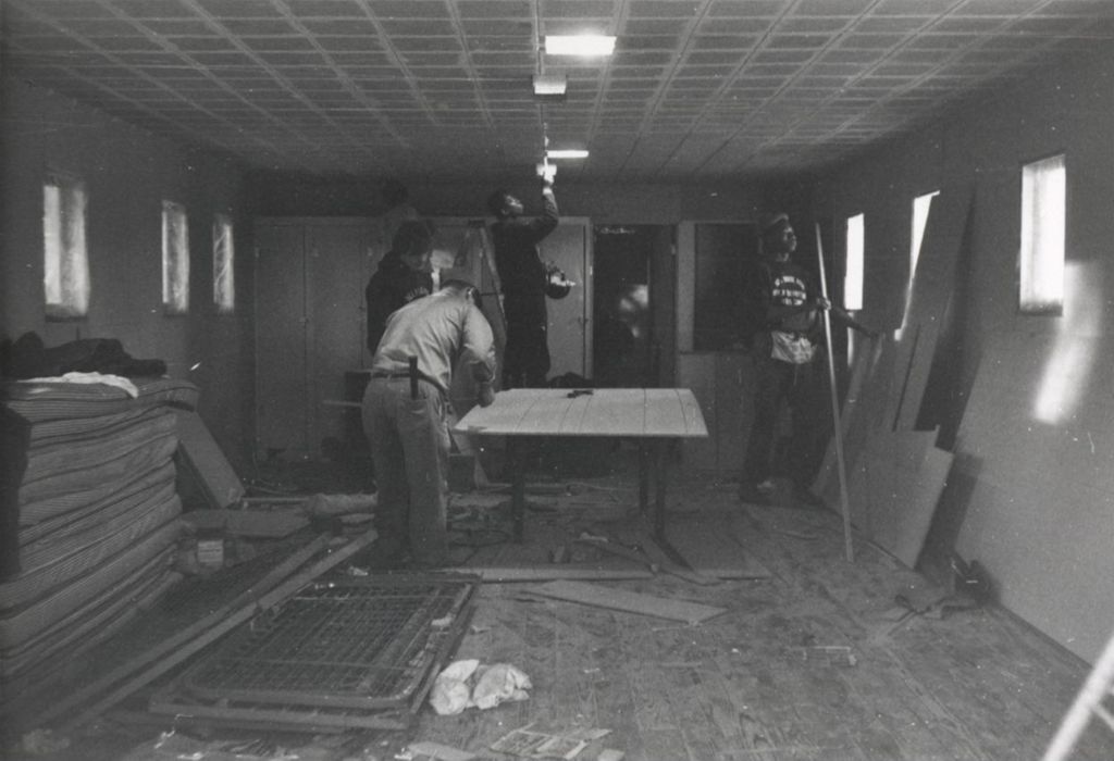 A man and three younger men doing construction in a room at the Hull-House camp in Wisconsin