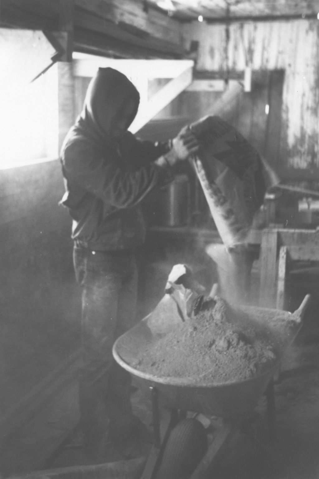Young man pouring dry cement into a wheelbarrow at the Hull-House camp in Wisconsin
