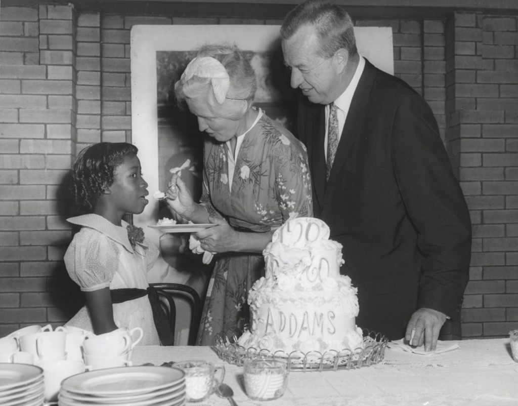 Miniature of Jane Addams' grand niece feeds a bite of cake celebrating the centennial of Addams' birth to a girl as the president of the Hull-House board looks on