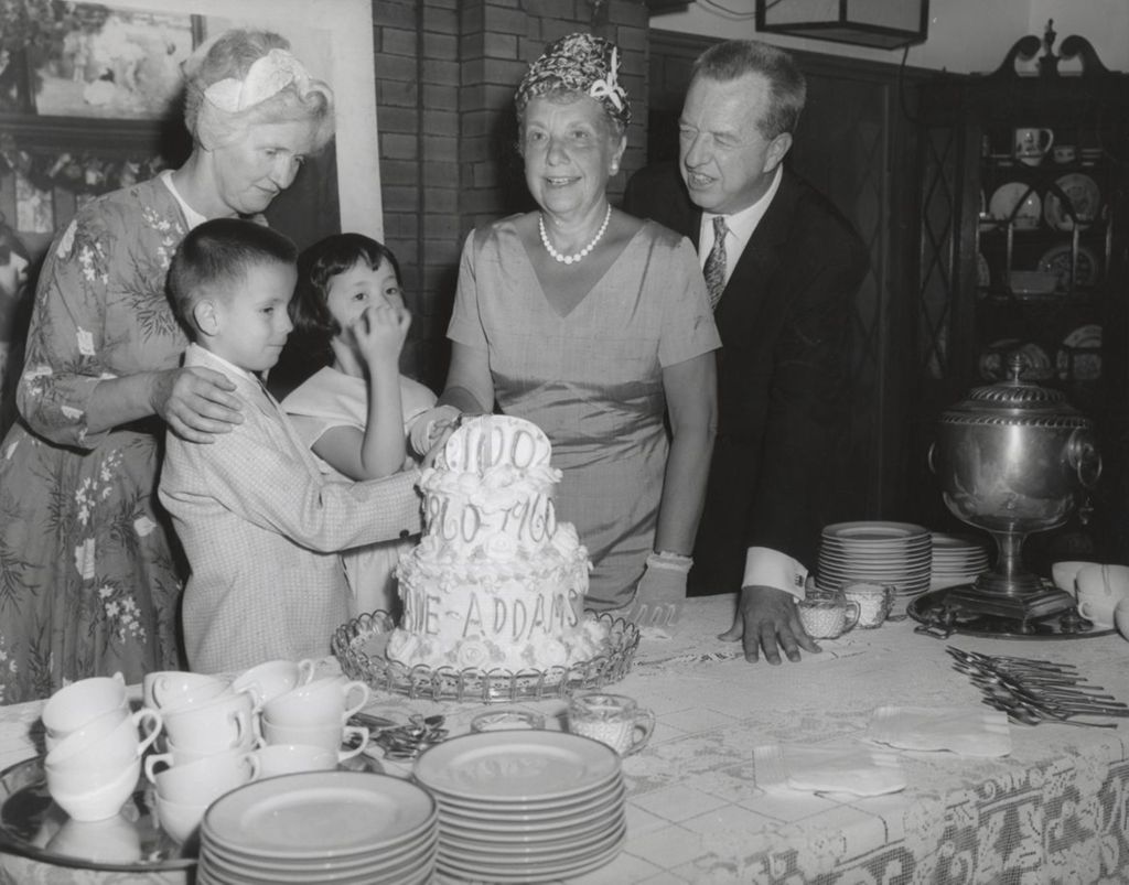 Two children and Congresswoman Marguerite Stitt Church cut into a cake celebrating the centennial of Jane Addams' birth; looking on are Jane Addams' grand niece and the president of the Hull-House board
