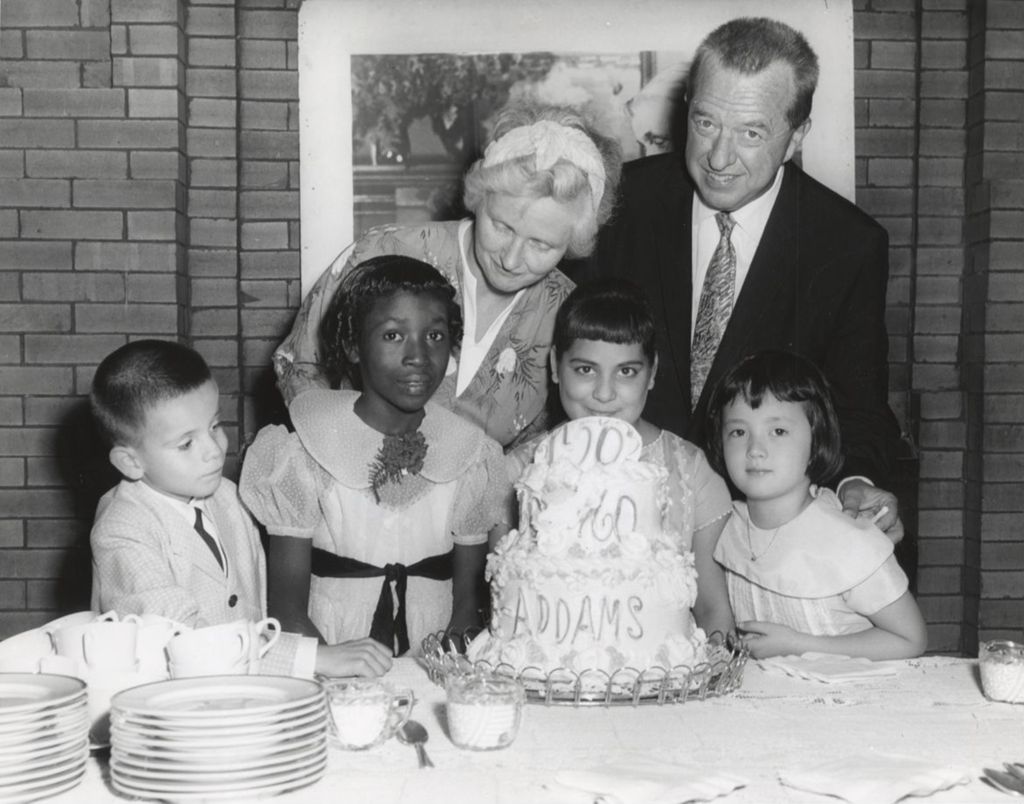 Four children and two adults (Jane Addams' grand niece and the president of the Hull-House board) pose with a cake celebrating the centennial of Jane Addams' birth
