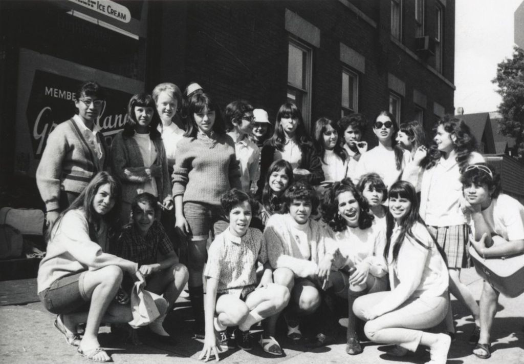 Miniature of Around 21 young women gathered for a "spring activity," posing next to a grocery store, likely near the Hull-House Jane Addams Center