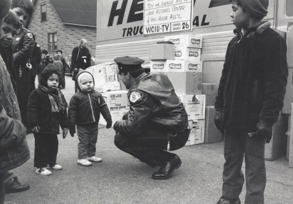 Police officer crouching to speak to two young children at a Hull-House Christmas toy giveaway