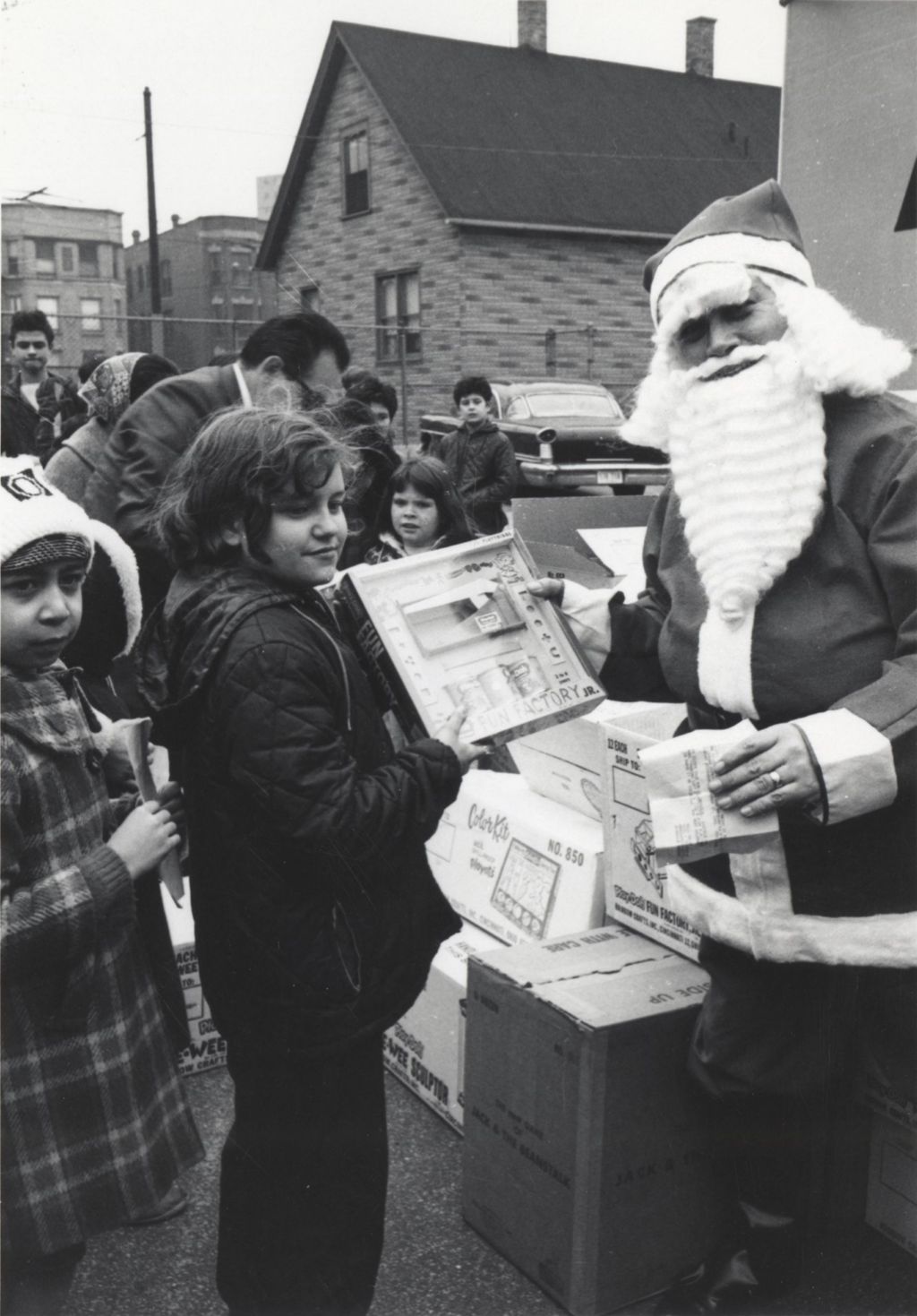 A man in a Santa Claus costume hands a present to a girl at a Hull-House Christmas toy giveaway