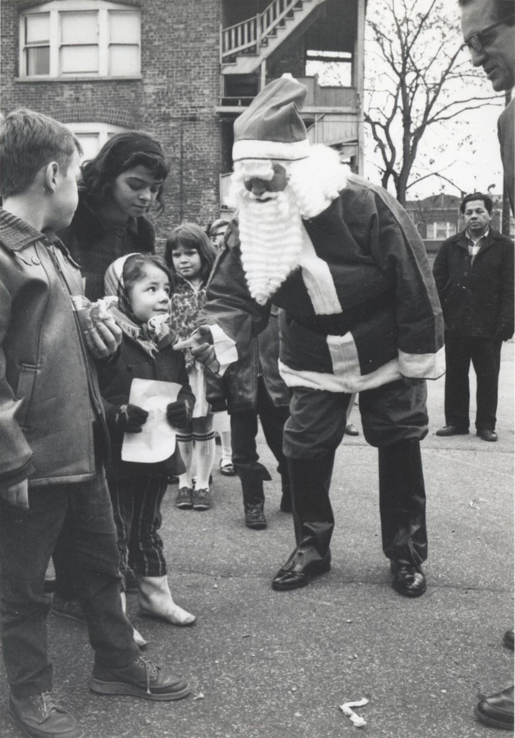 A man in a Santa Claus costume engages with a young girl at a Hull-House Christmas toy giveaway
