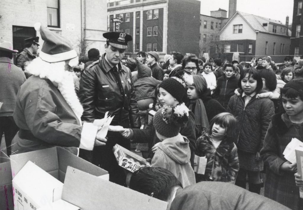 Man in Santa Claus costume giving toys to a crowd of children during a Hull-House Christmas toy giveaway