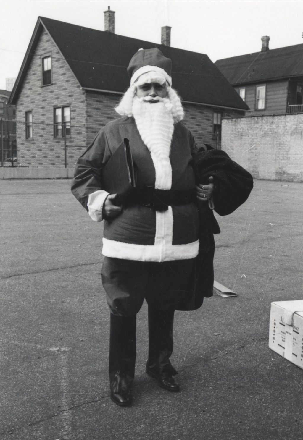 Man in Santa Claus costume standing in an empty lot for a Hull-House Christmas toy giveaway