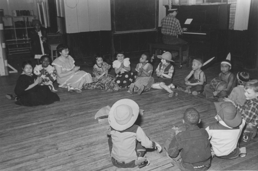A group of costumed children and an instructor sit in a circle on the floor during the 1951 Hull-House Spring Carnival