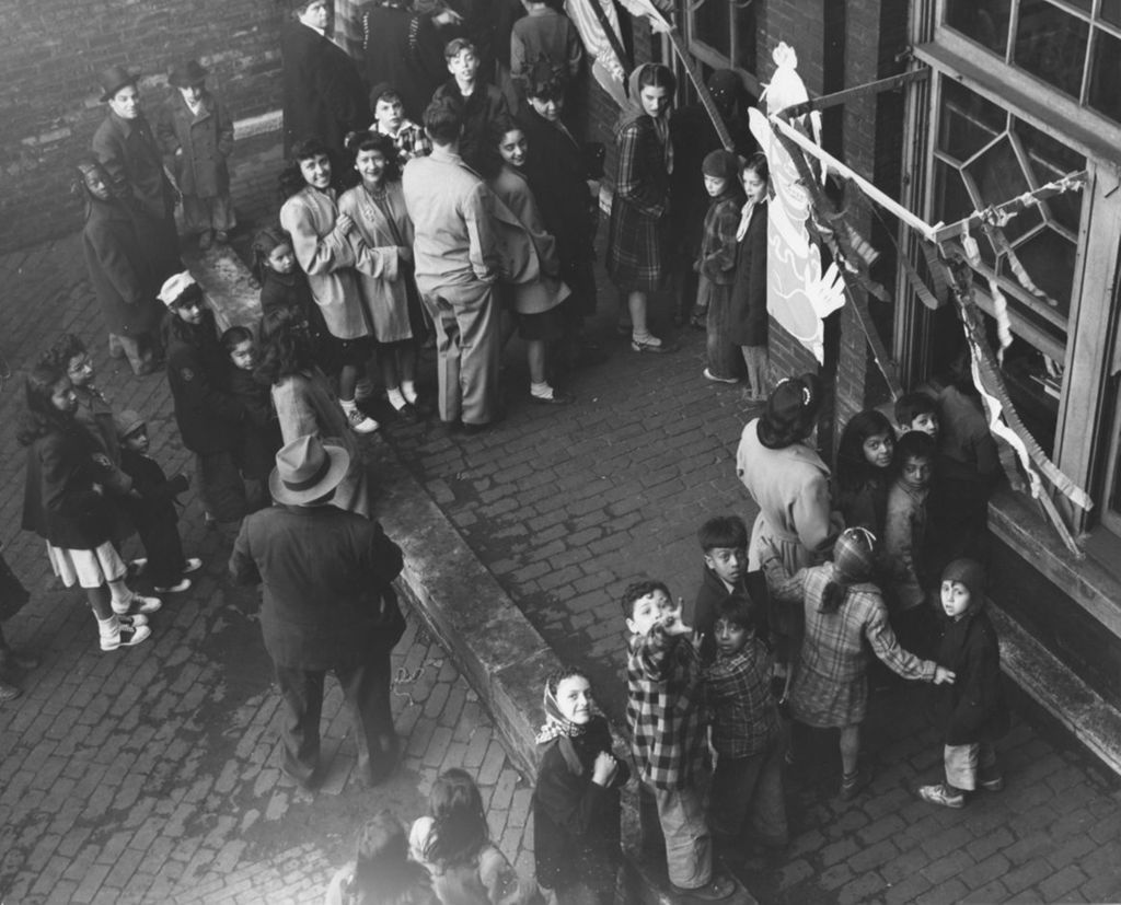 People lined up in the front courtyard of Hull-House to look inside windows during Hull-House Carnival