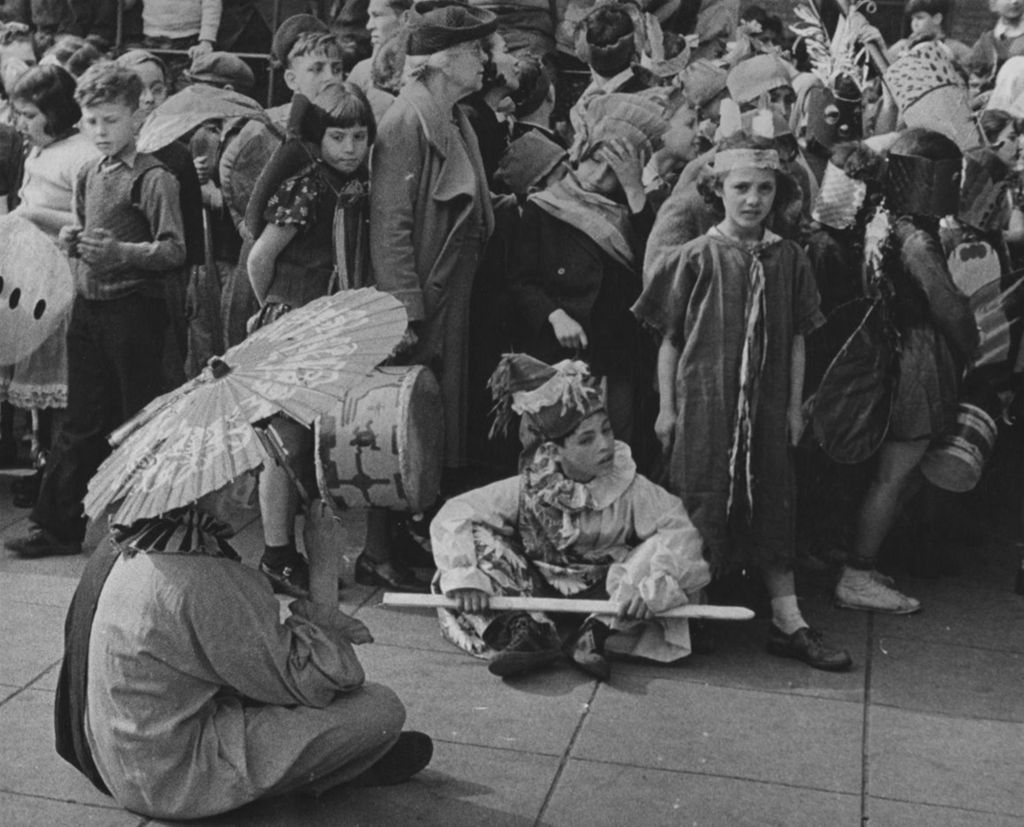 Two costumed young people sitting on the ground with crowd behind them during the Hull-House 50th Anniversary circus