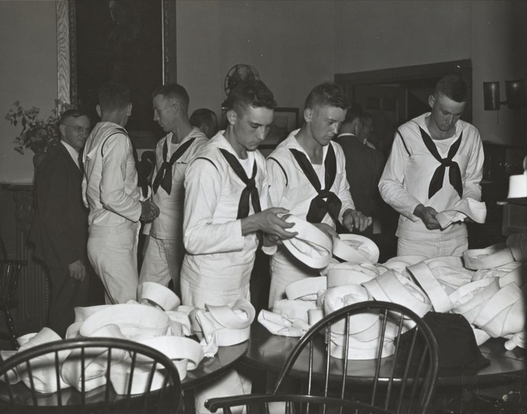 Three United States Navy sailors searching for their hats from a pile during an "Entertaining the Navy" event