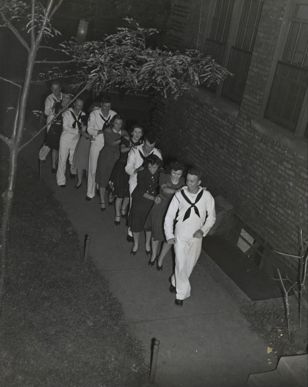United States Navy sailors in a conga line with several women in the Hull-House Courtyard during an "Entertaining the Navy" event
