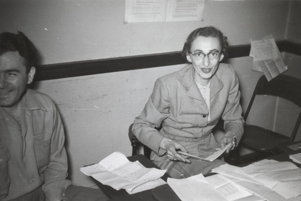 Hull-House program director Elaine Switzer sitting at a desk during a visit by Illinois governor Adlai Stevenson II