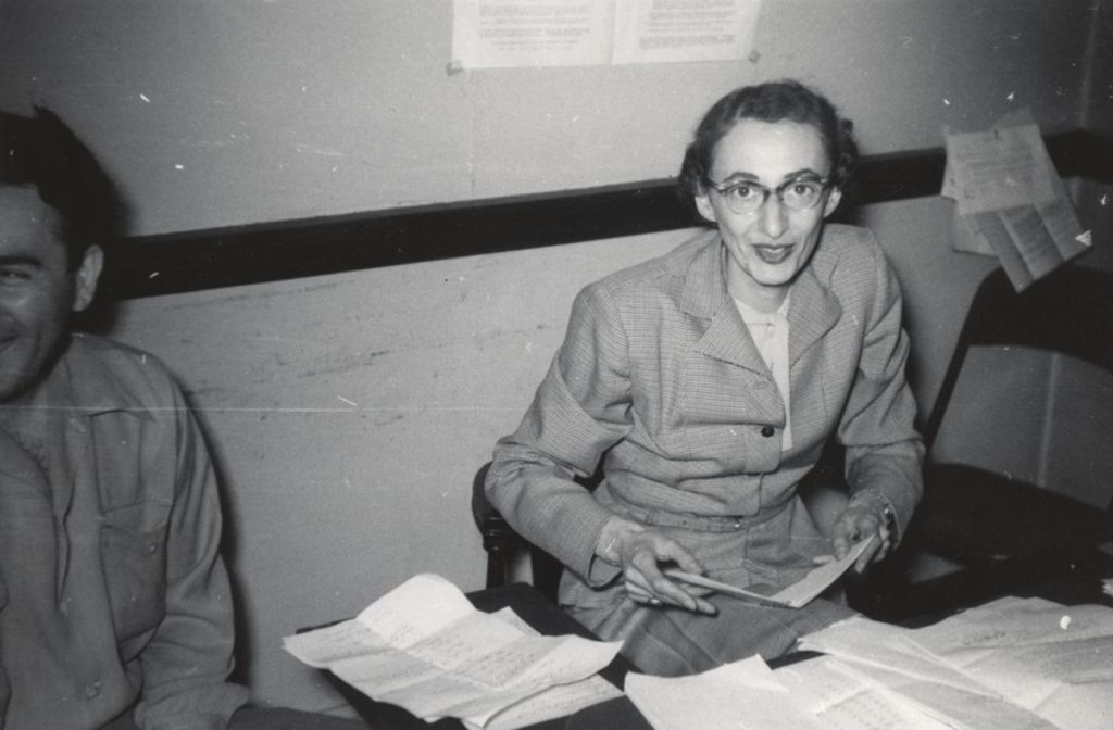 Hull-House program director Elaine Switzer sitting at a desk during a visit by Adlai Stevenson II