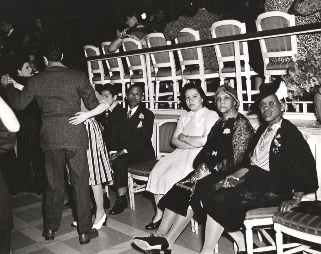 Attendees at the Lilac Ball sponsored by Hull-House sitting on chairs while some couples dance. Director Charlotte Carr insisted that African Americans be invited to the Ball
