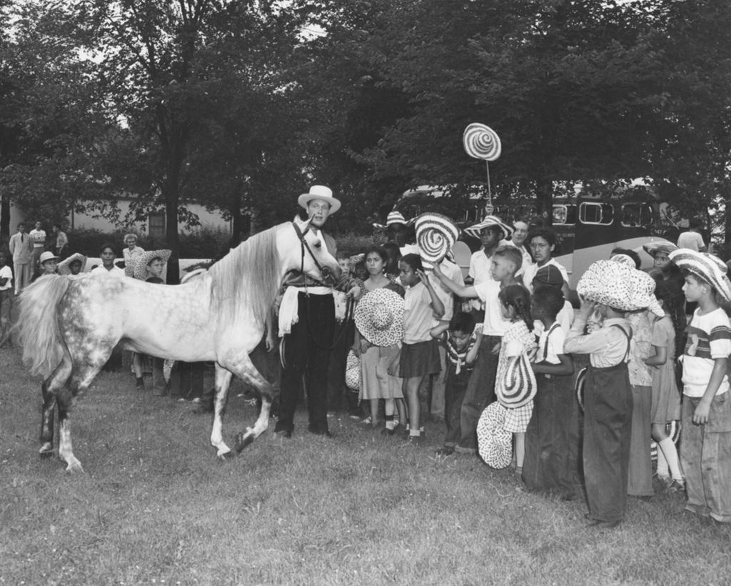 Miniature of Man dressed as a cowboy shows a horse to assembled children from Hull-House during a trip to Hawthorn-Mellody Farms