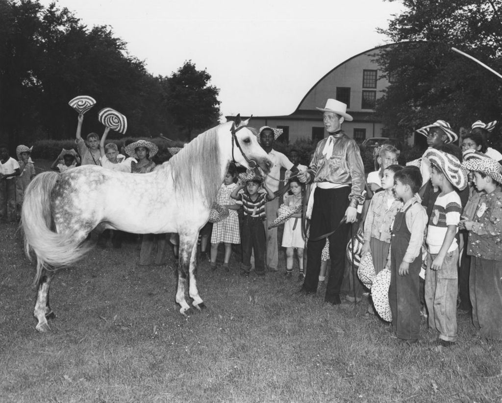Children from Hull-House stand around a horse and a man dressed as a cowboy during a trip to Hawthorn-Mellody Farms