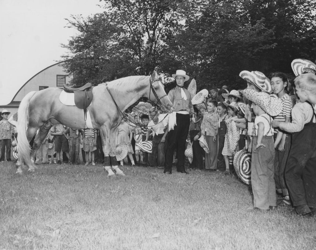 Dozens of children stand around a horse and a man dressed as a cowboy during a Hull-House trip to Hawthorn-Mellody Farms