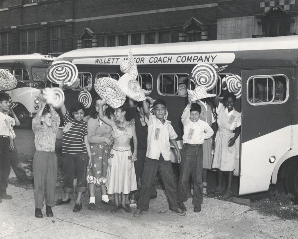 Twelve children waving sombreros outside a bus at Hull-House in connection with a trip to Hawthorn-Mellody Farms