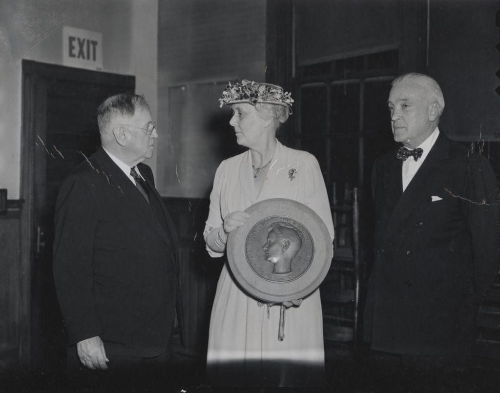 Hull-House board president Alma Petersen stands between Harold Ickes and Marshall Field III holding a plaque honoring Louise de Koven Bowen at the 1949 Associates Dinner