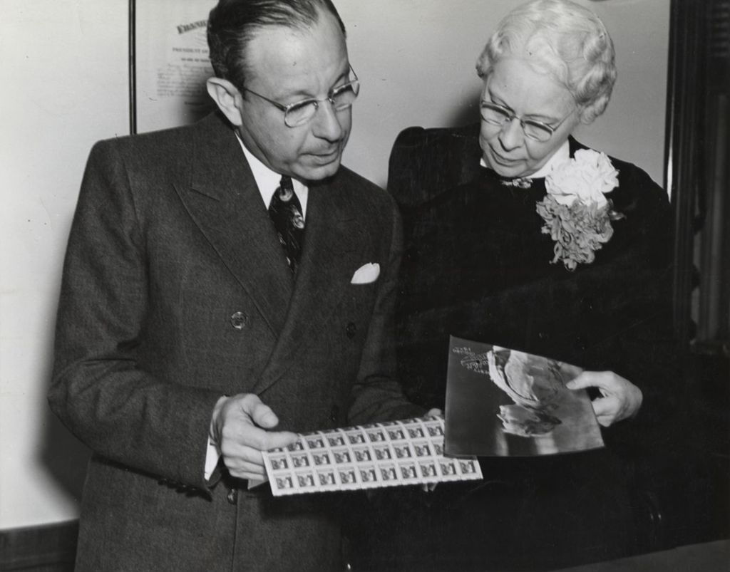 Miniature of Film producer Charles R. Rogers holding a sheet of newly issued Jane Addams 10-cent stamps alongside Mary Briggs, Los Angeles Postmistress, who is holding a photo portrait of Addams
